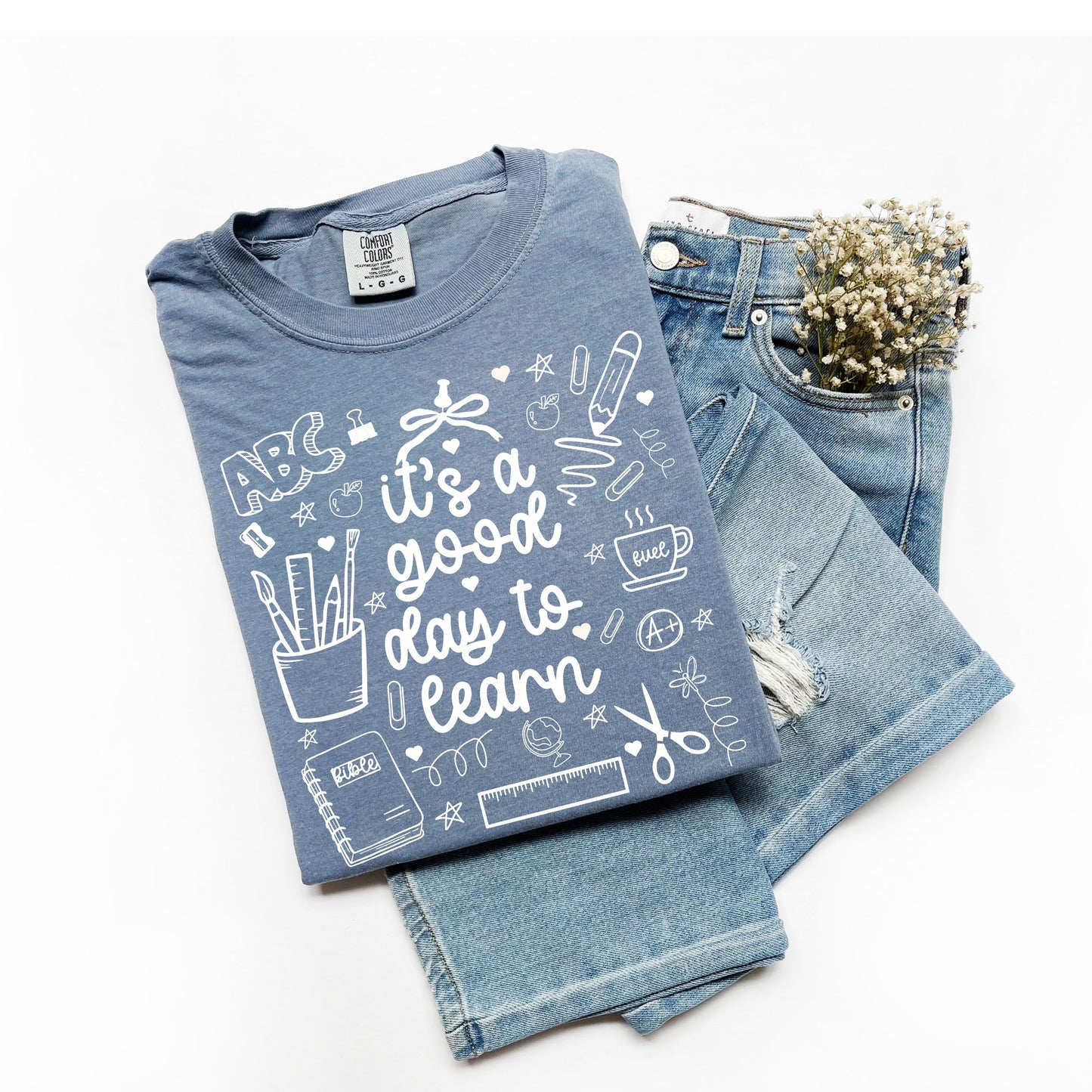Folded blue t-shirt with educational graphics and text, paired with denim jeans on a white background.