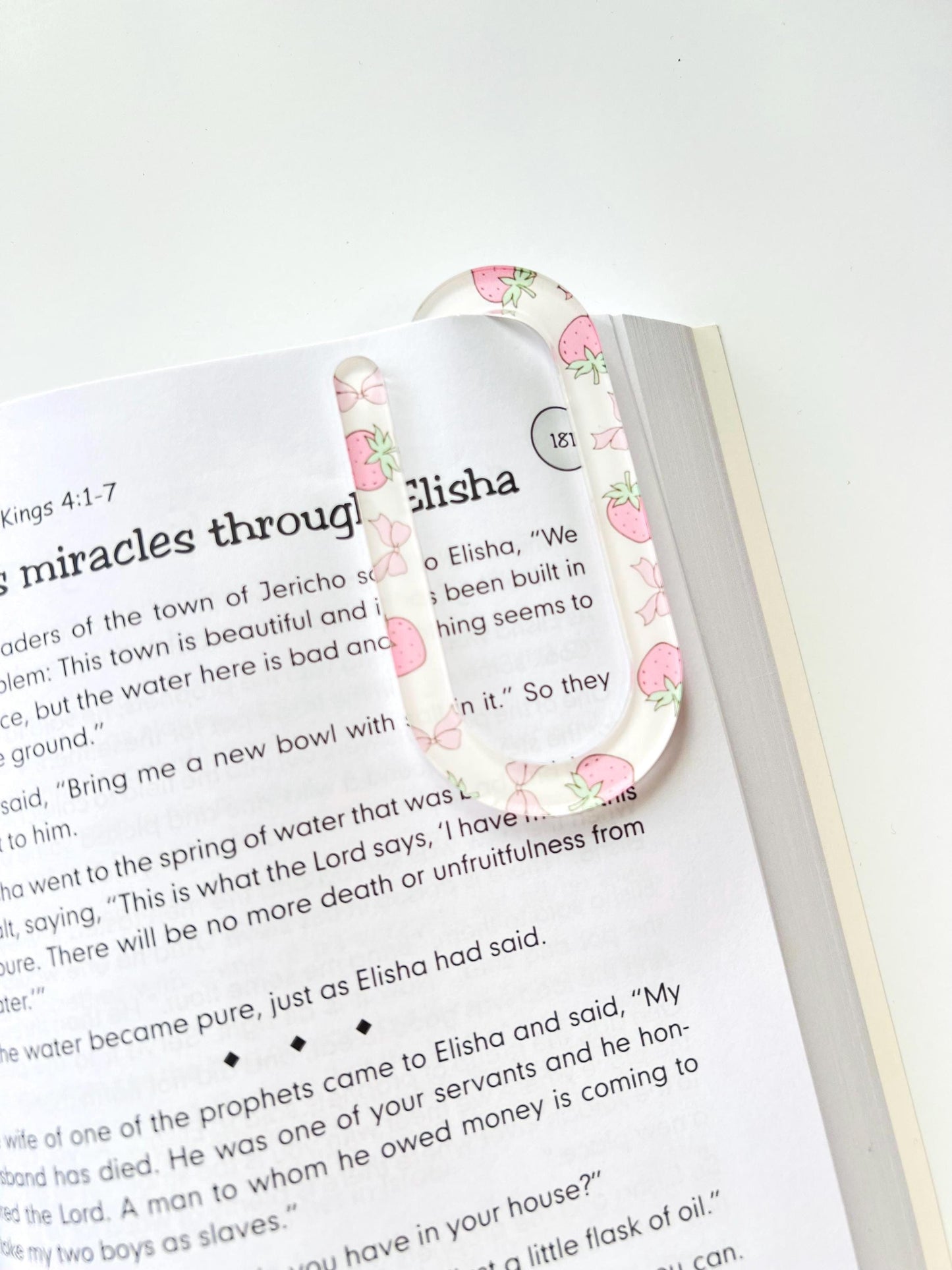 Clear acrylic bookmark with pink strawberry pattern clipped onto an open Bible at 2 Kings 4