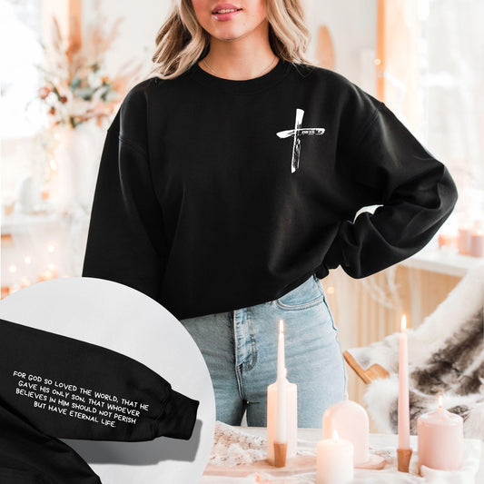 Woman wearing a black John 3:16 Hoodie with a white brushstroke cross and John 3:16 on the chest, with scripture detail on the sleeve