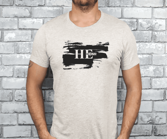 Man wearing a heather dust Christian t-shirt with bold black brushstroke and “He Reigns” text, inspired by Psalm 9:7.