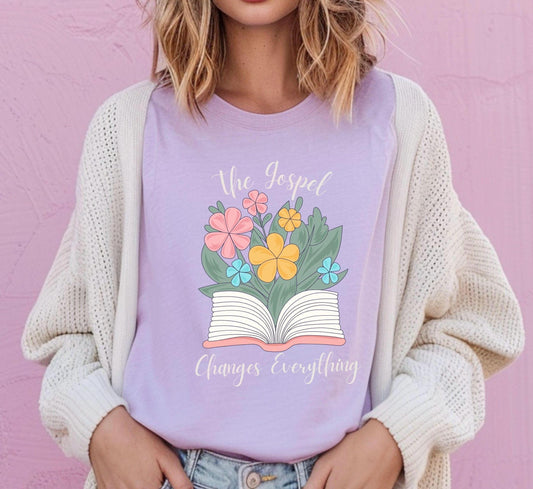 Woman wearing blue jean Comfort Colors t-shirt with The Gospel Changes Everything floral Bible design by Abound in Faith