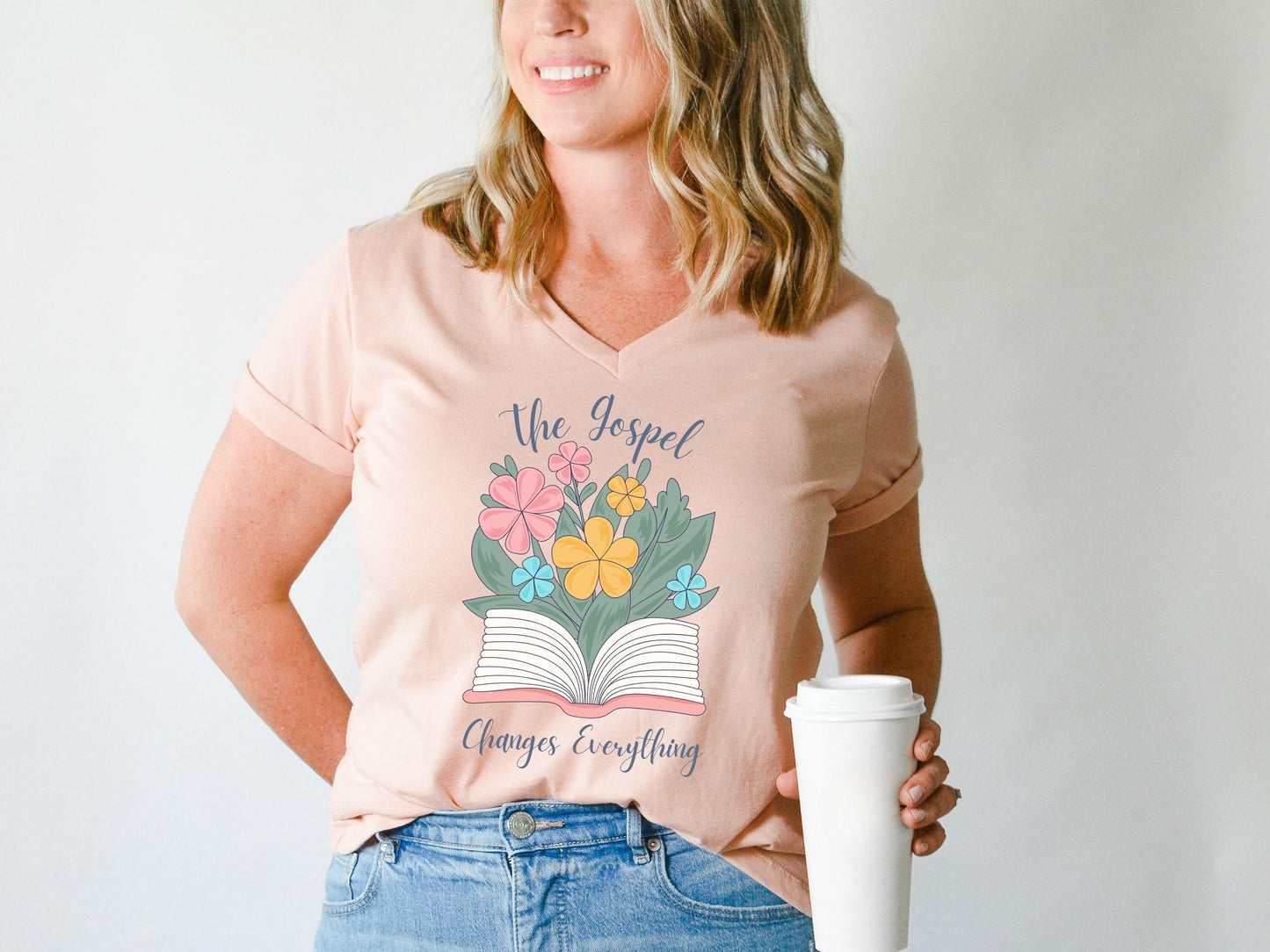Woman wearing peach Bella canvas V-neck t-shirt with The Gospel Changes Everything floral Bible design by Abound in Faith