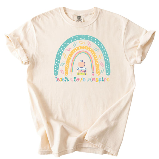Flat lay of a pastel rainbow teacher t-shirt with the phrase ‘Teach Love Inspire’ and paperclip accents.