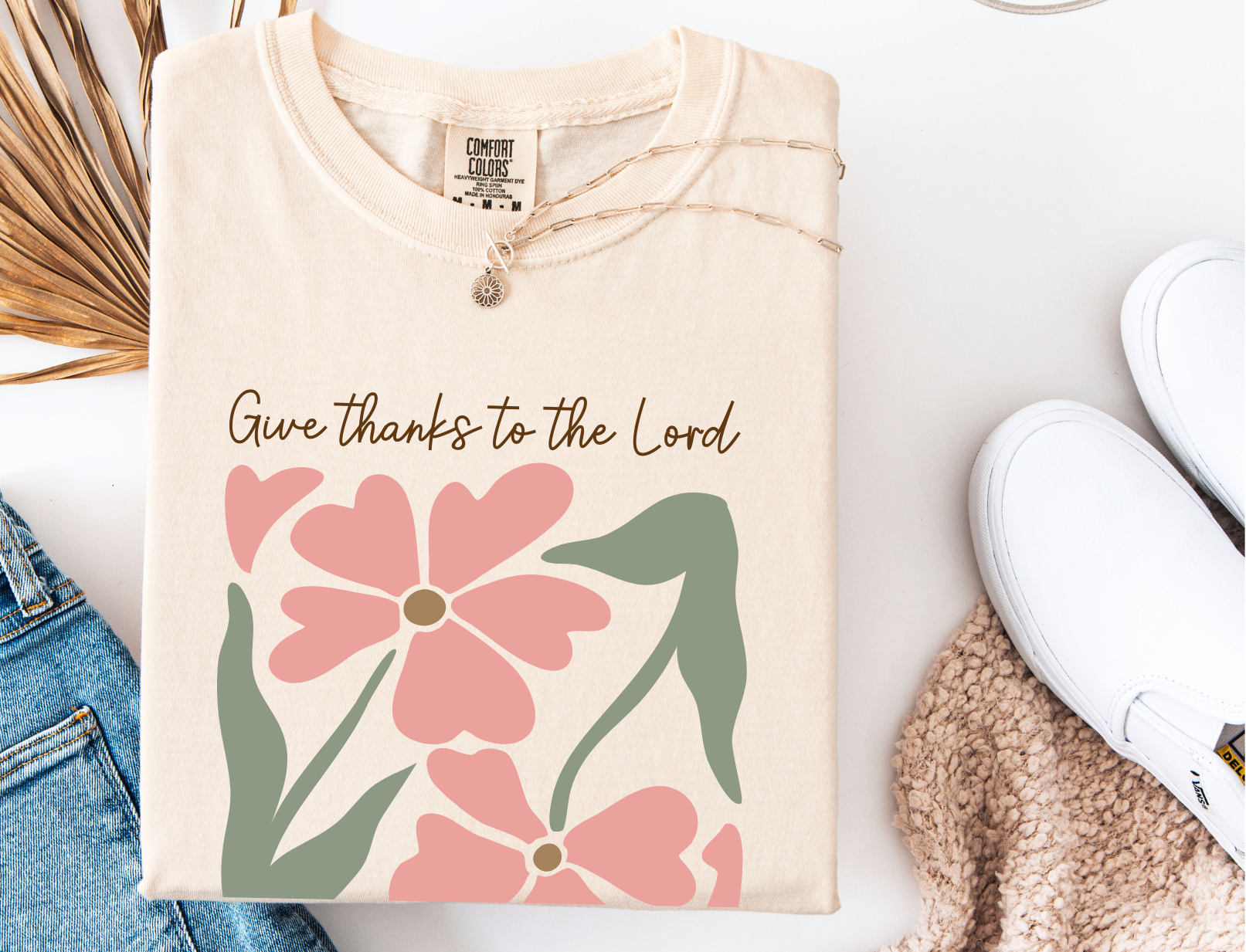 Beige sweatshirt with floral design and 'Give thanks to the Lord' text on a white surface.