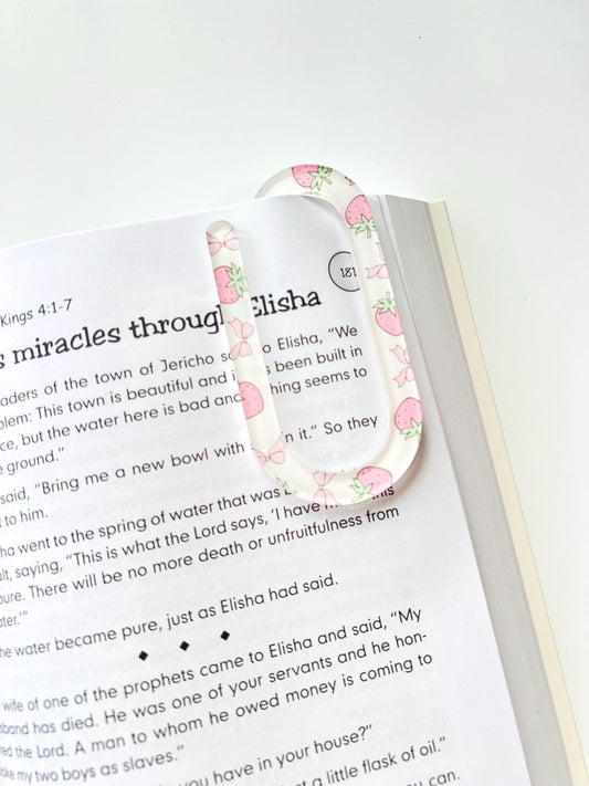 Clear acrylic bookmark with pink strawberry pattern clipped onto an open Bible at 2 Kings 4
