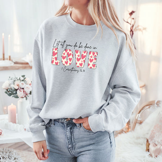 Woman wearing Let all that you do be done in love sweatshirt with heart-filled “LOVE” lettering and scripture from 1 Corinthians 16:14.