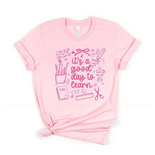 Flat lay of ivory “It’s a Good Day to Learn” teacher shirt with light blue design for back to school.